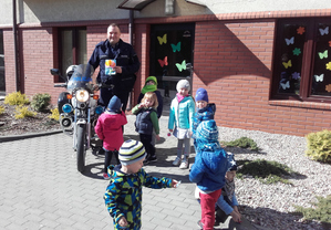Policjant stoi przy grupie dzieci i motocyklu służbowym