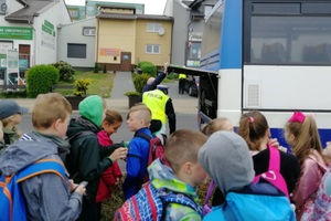 Dzieci czekają na upragniony wyjazd, a policjant sprawdza stan silnika autokaru.