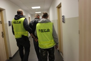 Policjanci prowadzą korytarzem komendy w Toruniu zatrzymanego autora fałszywych alarmów bombowych