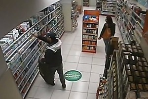 Po lewej stronie mężczyzna z dużym czarnym workiem ściąga z półki kosmetyki, a kobieta chodzi po sklepie.