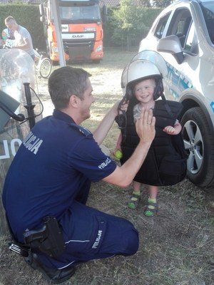 Policjant przybija &quot;piątkę&quot; z uśmiechniętym dzieckiem, który ma hełm na głowie i kamizelkę policyjną