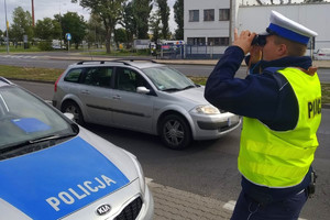 policjant wypatruje przez lornetkę kierowców korzystających z telefonów komórkowych podczas jazdy