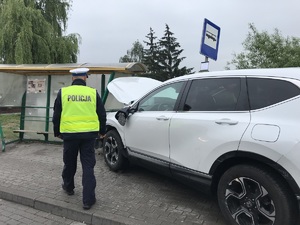 Policjant stoi nad rozbitym samochodem