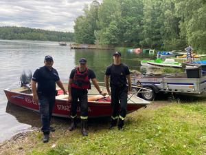 Policjant i strażacy stoją przy łódce na tle jeziora