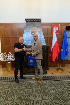 Spotkanie w Ambasadzie Polskiej w Berlinie z Rafałem Hokuszem. W tle kominek i flaga Polski i Unii Europejskiej.