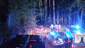 Widok na rozbity samochód i służby ratunkowe pracujące w okolicy wypadku