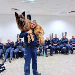 Policjant niosący psa na ramionach.
