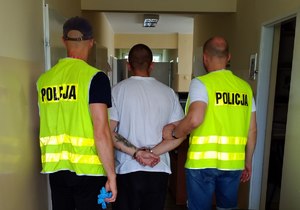 Policjanci prowadzą zatrzymanego korytarzem komisariatu.