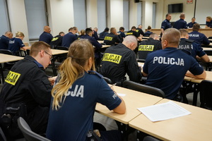 policjanci na sali odpraw siedzą i notują zadania do służby