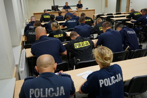 policjanci siedzą na sali odpraw i notują zadania do służby