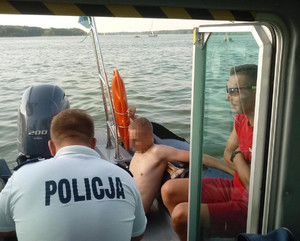 Załoga policyjnej łodzi motorowej oraz mężczyzna wyciągnięty z wody odpoczywa na łodzi.