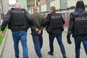 policjanci prowadzą zatrzymanego skutego kajdankami