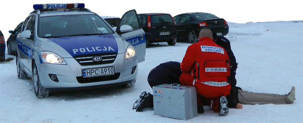 Policjant i ratownik medyczny udzielają pomocy osobie leżącej na śniegu.