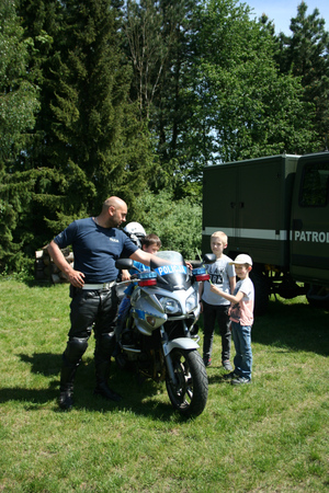 Chłopiec siedzi na policyjnym motocyklu, w pobliżu stoją dwaj inni chłopcy, a obok policjant &quot;drogówki&quot;.