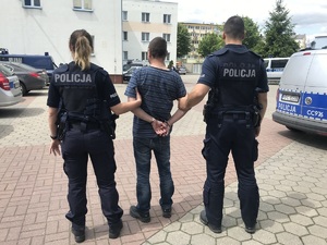 Drugi z zatrzymanych prowadzony przez policjantów przez dziedziniec komendy.