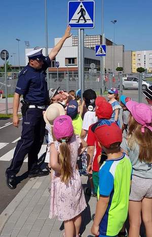 Policjant wskazując na znak uczy jak przechodzić w miejscu do tego wyznaczonym.