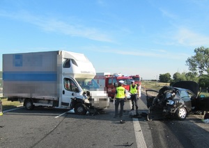 Policjanci stoją pomiędzy roztrzaskanymi dwoma autami, a w tle dwa wozy strażackie