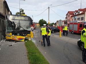 Na pierwszym planie rozbity autobus. Policjanci robią oględziny.