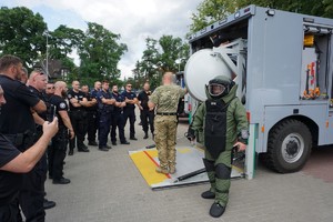 Policjanci oglądają specjalistyczny samochód do przewozu ładunków wybuchowych i kombinezon  przeciwwybuchowy