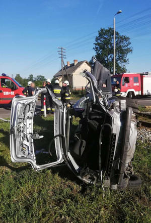 Auto, w które uderzył pociąg, a w tle strażacy.