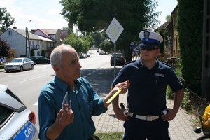 Pieszy rozmawia z policjantami trzymając opaskę odblasskową