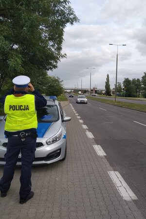 policjant wypatruje przez lornetkę kierowców korzystających z telefonów komórkowych podczas jazdy