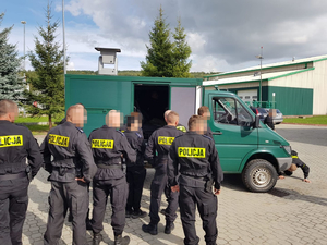 kilku policjantów stoi przed zielonym samochodem