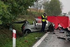 Policjant robi oględziny rozbitego peugeota stojącego za parawanem