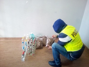 Policjant przekłada worki z krajanką, a obok stoją butelki z alkoholem bez polskiej akcyzy