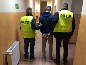 Policjanci prowadzą korytarzem podejrzanego o oszustwa finansowe