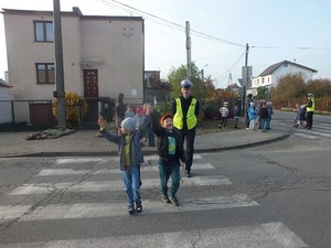 Policjant przeprowadza dzieci przez jezdnię na przejściu dla pieszych