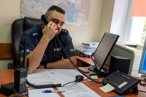 policjant siedzi przy biurku i rozmawia przez telefon