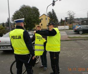 Policjant RD i strażnik gminny rozmawiają z rowerzystką i prezentują kamizelkę odblaskową