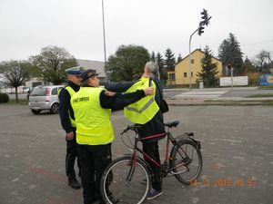 Policjant RD i strażnik gminny rozmawiają z rowerzystą, który zakłada kamizelkę odblaskową