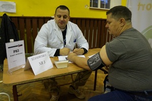 mężczyzna siedzi przy biurku i mierzy ciśnienie krwi