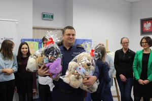 Policjant trzyma przekazane misie. W tle inni uczestnicy spotkania.