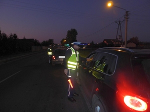 Na pierwszym planie policjant RD podaje AlcoBlow kierowcy, a w tle inny funkcjonariusz kontroluje kierowcę poprzedzającego auta