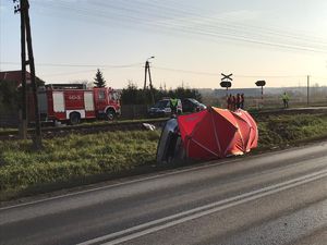 Citroen leży na boku przysłonięty parawanem, w oddali stoi wóz straży pożarnej i policji