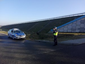 Policjant mierzy prędkość auta, a obok stoi radiowóz