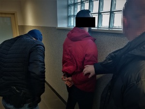 Zatrzymany stoi i patrzy w okno, obok policjanci operacyjni