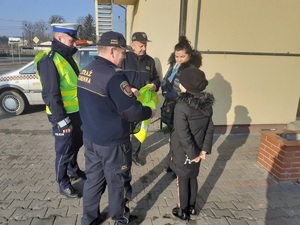 Strażnicy gminni i policjant rozmawiają z dziewczynką, której za chwilę podarują kamizelkę