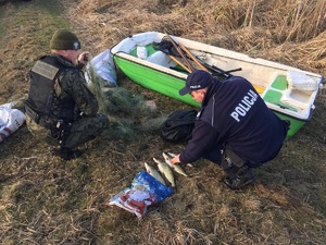 Strażnik rybacki trzyma sieci, a policjant wskazuje na cztery złowione szczupaki