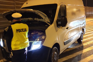 Policjant sprawdza stan silnika w białym dostawczaku