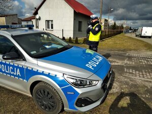 Policjant stoi przy radiowozie i mierzy prędkość