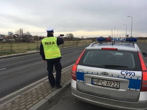 Policjant RD stoi obok radiowozu i mierzy prędkość nadjeżdżających pojazdów