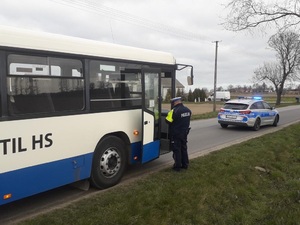 Policjant podczas kontroli autobusu. W tle widoczny radiowóz.