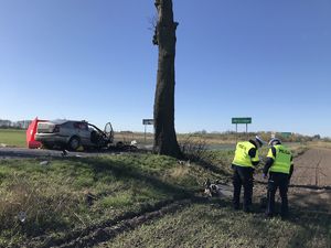 Miejsce zdarzenia. Rozbite auto w tle. Policjanci wykonują czynności.