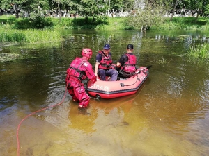 Policjant i strażak siedzą na pontonie, a kolejny go woduje