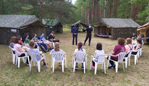 Uczestnicy obozu siedzą a przed nimi stoją mundurowi