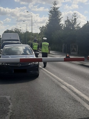 Policjanci kontrolują zatrzymane samochody przy przejeździe kolejowym